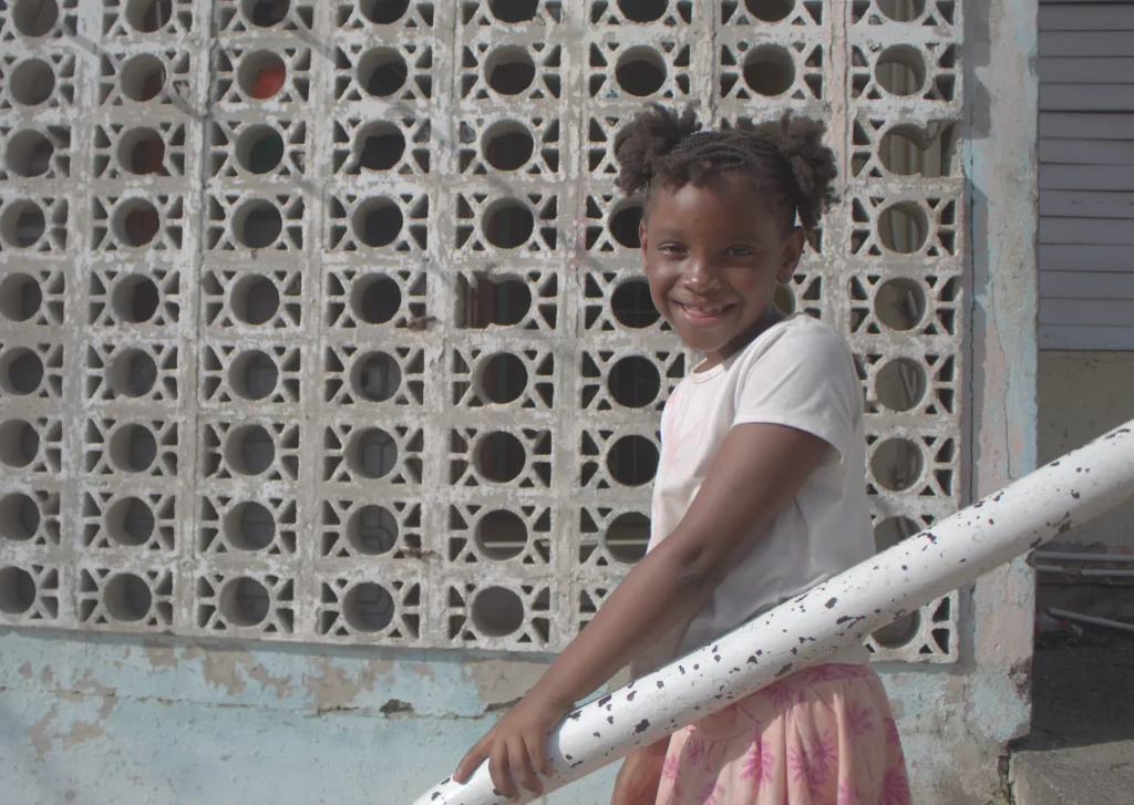 Smiling child standing by a railing during the Give Back in Trench Town, Jamaica.