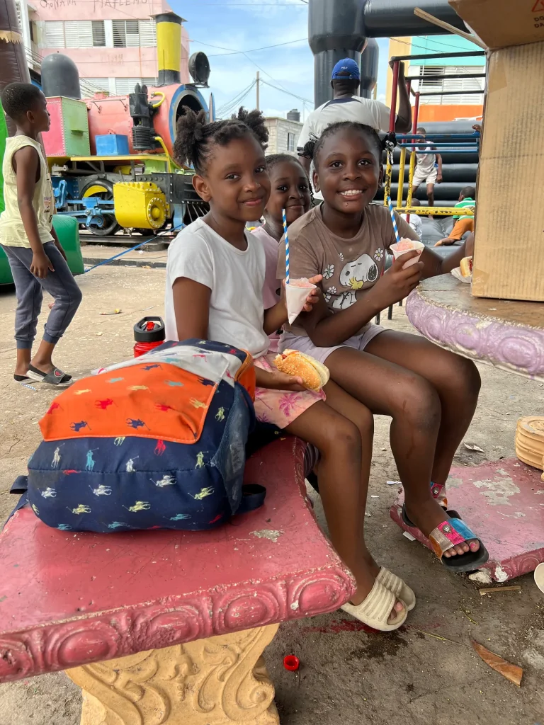Children smiling together during the Chuchu Benz Foundation Give Back in Trench Town, Jamaica, with the colorful train behind them.